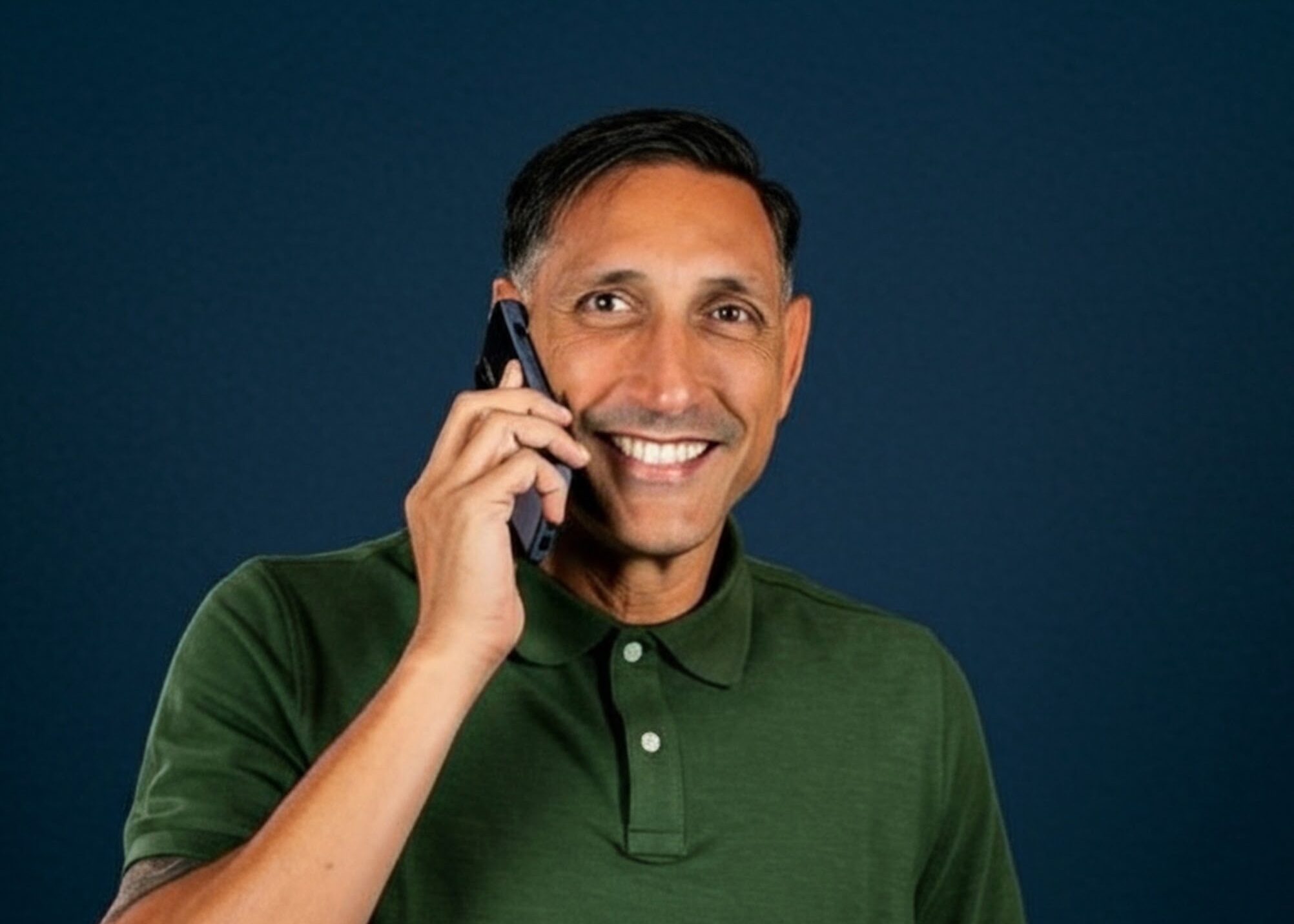 Jarrod Roberts smiling with a mobile phone held to his ear mid-call, against a deep navy background.