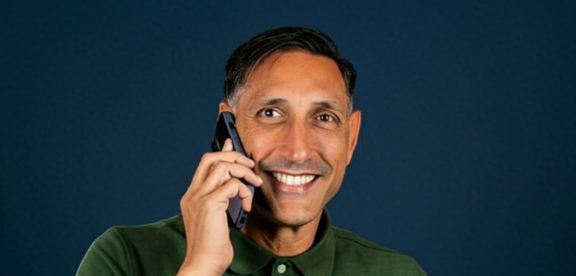 Jarrod Roberts smiling with a mobile phone held to his ear mid-call, against a deep navy background.