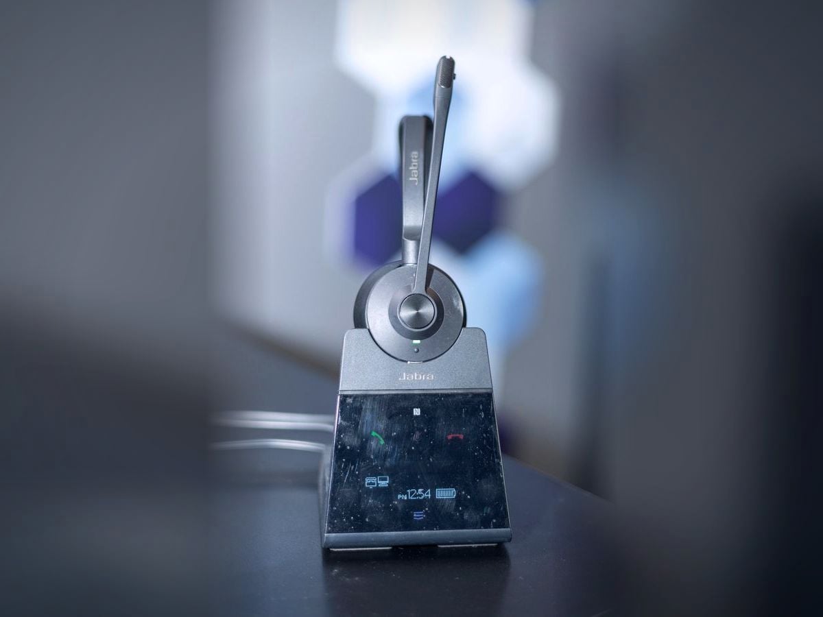 A wireless headset standing on its charging base, photographed close with a soft background.