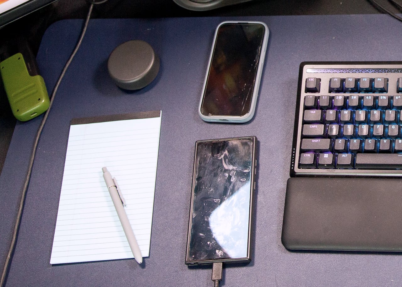 Overhead view of a sales desk: notepad, pen, phones and keyboard.