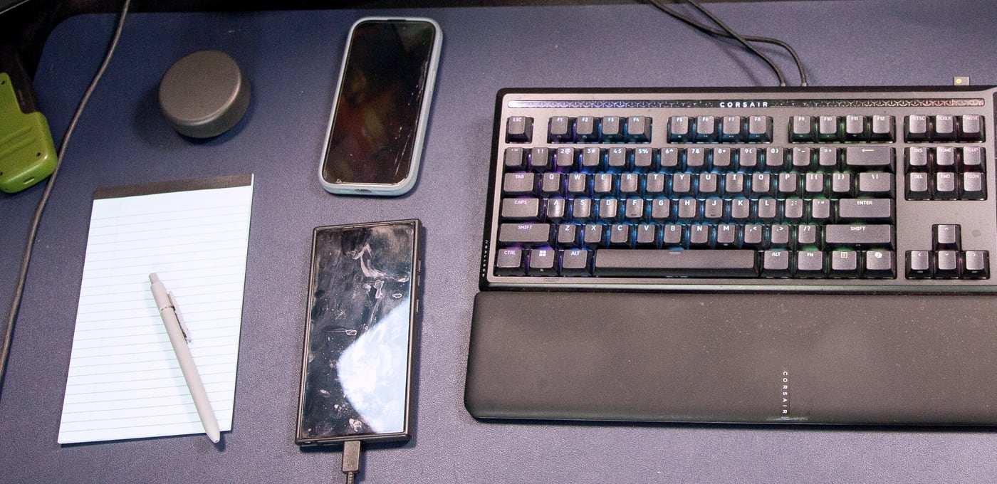 Overhead view of a sales desk: notepad, pen, phones and keyboard.