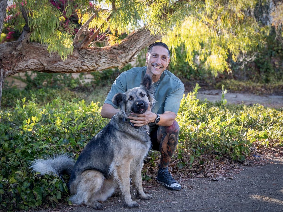 Jarrod Roberts crouching on a garden path with his dog Dodger, both looking at the camera.