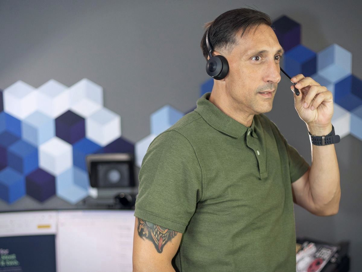 Jarrod Roberts in a headset adjusting the microphone, standing in his home sales office.